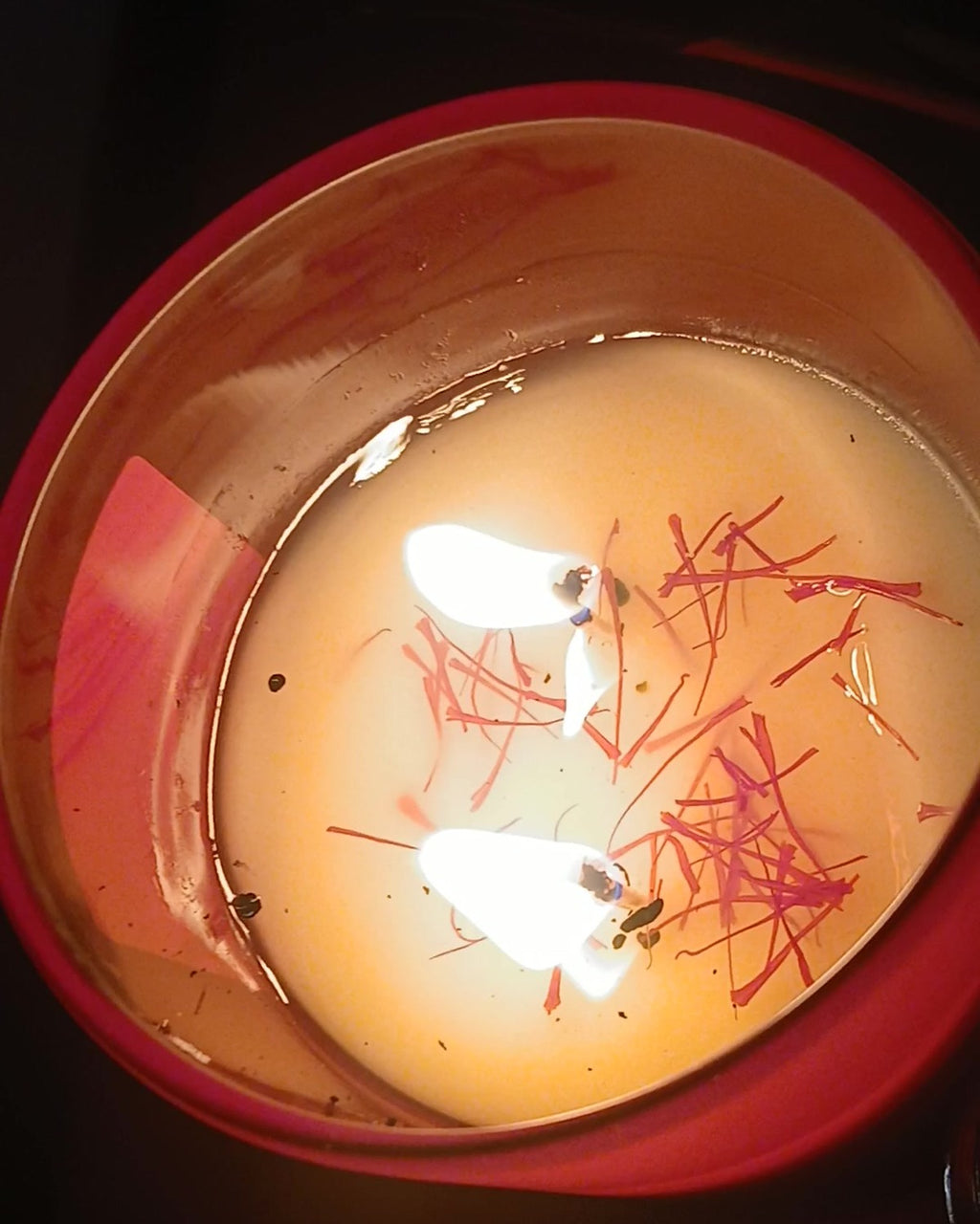 Saffron and sparkling wine candle burning in a silver tin, real saffron threads visible in the melted wax